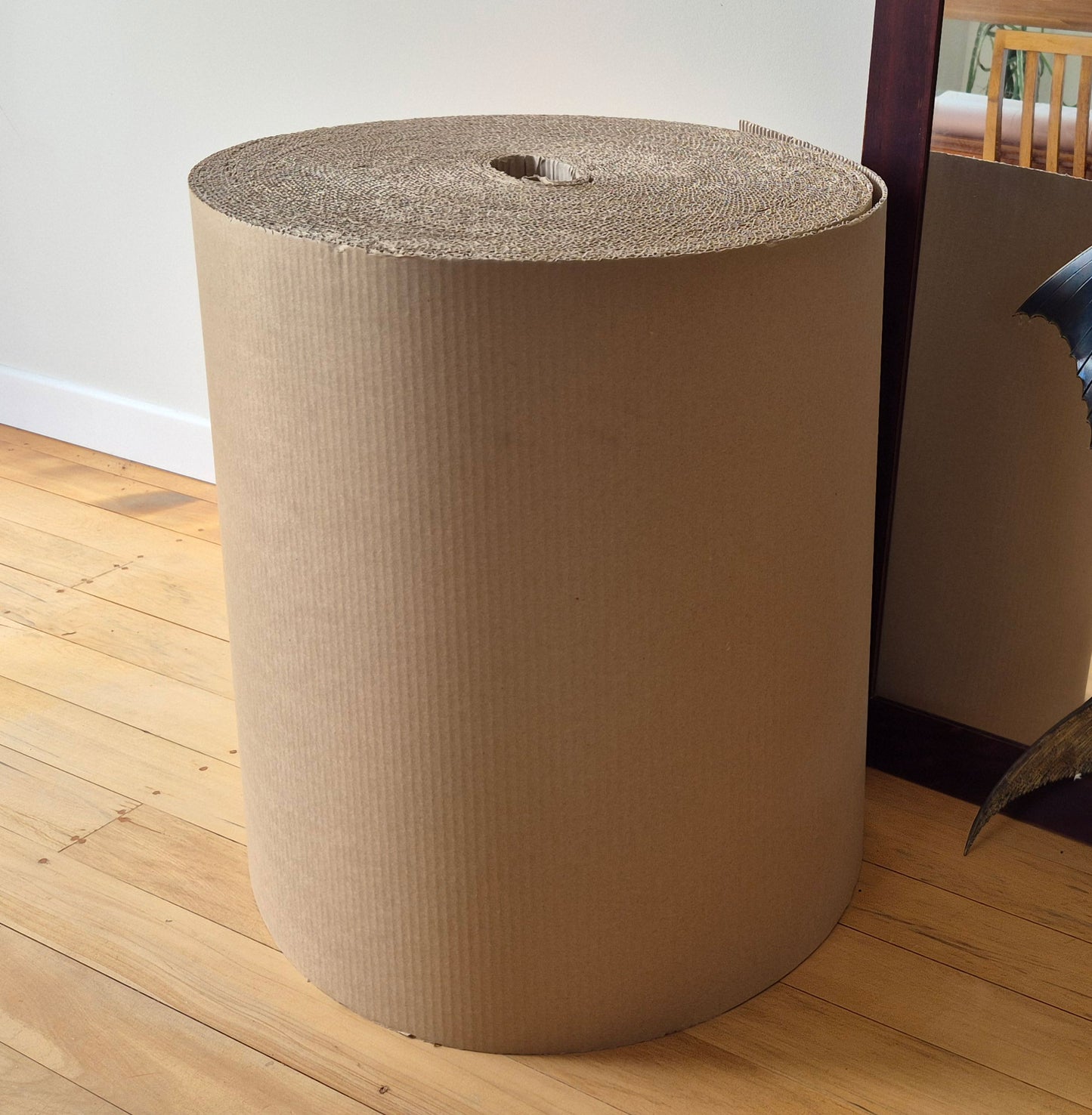 Cardboard roll on a wooden floor with a white wall in the background